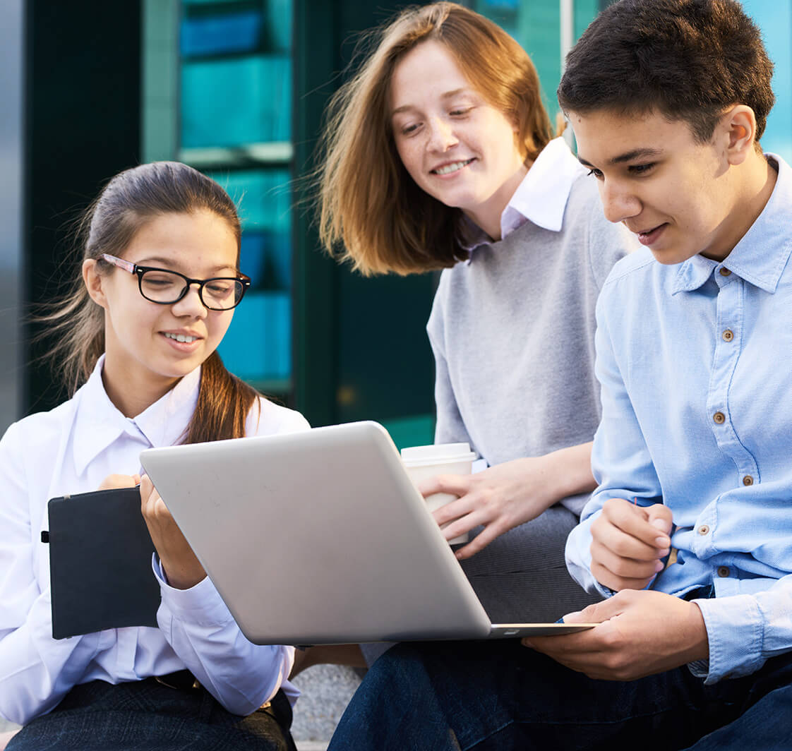 Group of children using laptop by school building.